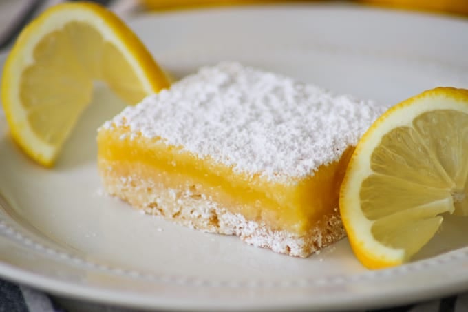 Easy Lemon Bar on a white plate with a lemon slice on each side.