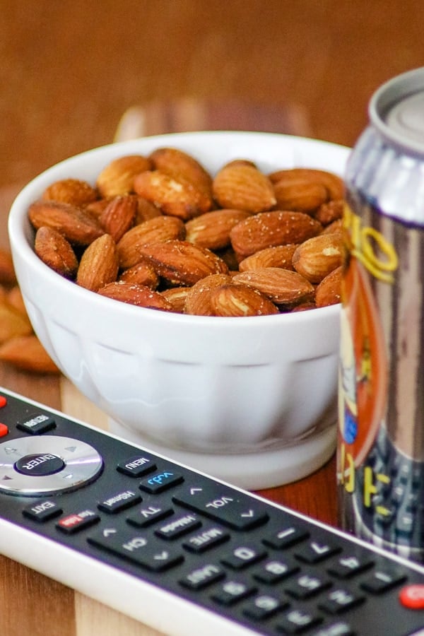 TV remote, can of beer with a bowl of Baked Spiced Almonds in background.