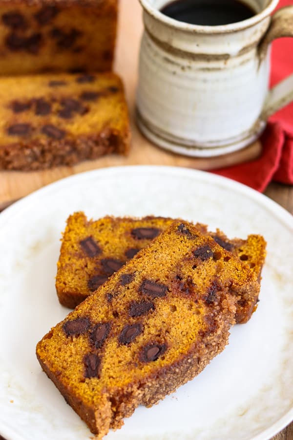 Two slices of Chocolate Chunk Pumpkin Bread on a plate with a mug of coffee.