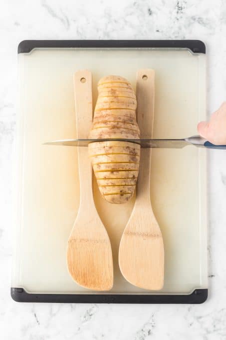 Slicing through a potato with wooden spoons preventing cuts all the way through.