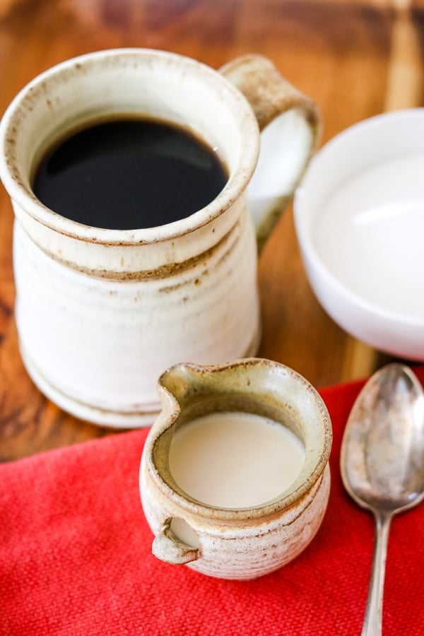 A cup of coffee, a spoon, a sugar bowl and Homemade French Vanilla Coffee Creamer.