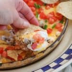 This Taco Dip is an easy game day dish to make, and fun to serve. The four layers of deliciousness are sure to please your hungry crowd. This dip of refried beans, taco seasoned ground beef, sour cream and Mexican cheese topped with diced tomato, jalapeño, and served with tortilla chips is a fan favorite at our house!