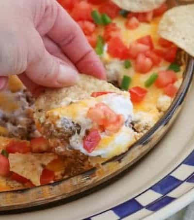 This Taco Dip is an easy game day dish to make, and fun to serve. The four layers of deliciousness are sure to please your hungry crowd. This dip of refried beans, taco seasoned ground beef, sour cream and Mexican cheese topped with diced tomato, jalapeño, and served with tortilla chips is a fan favorite at our house!