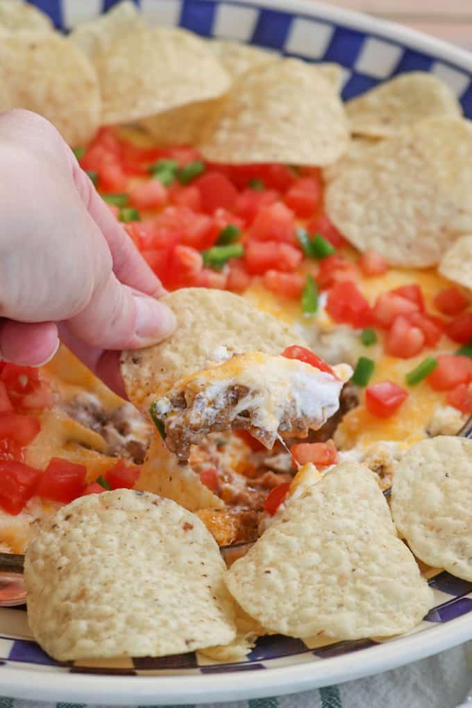 This Taco Dip is an easy game day dish to make, and fun to serve. The four layers of deliciousness are sure to please your hungry crowd. This dip of refried beans, taco seasoned ground beef, sour cream and Mexican cheese topped with diced tomato, jalapeño, and served with tortilla chips is a fan favorite at our house!