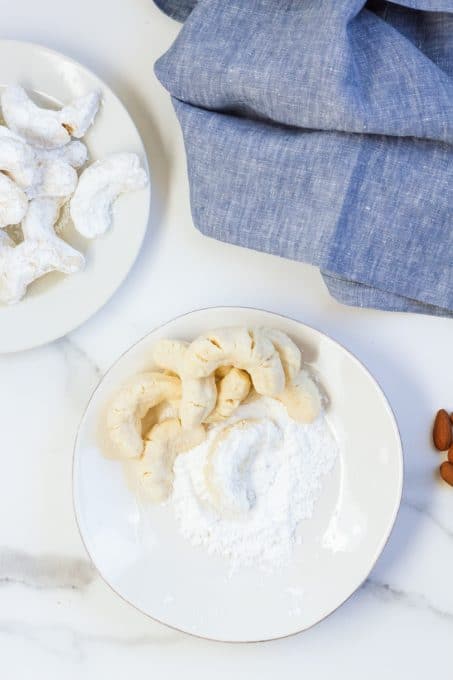 Almond crescent cookies being coated in powdered sugar.