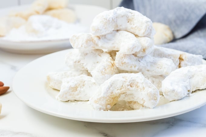 A plate full of almond cookies dusted with powdered sugar.