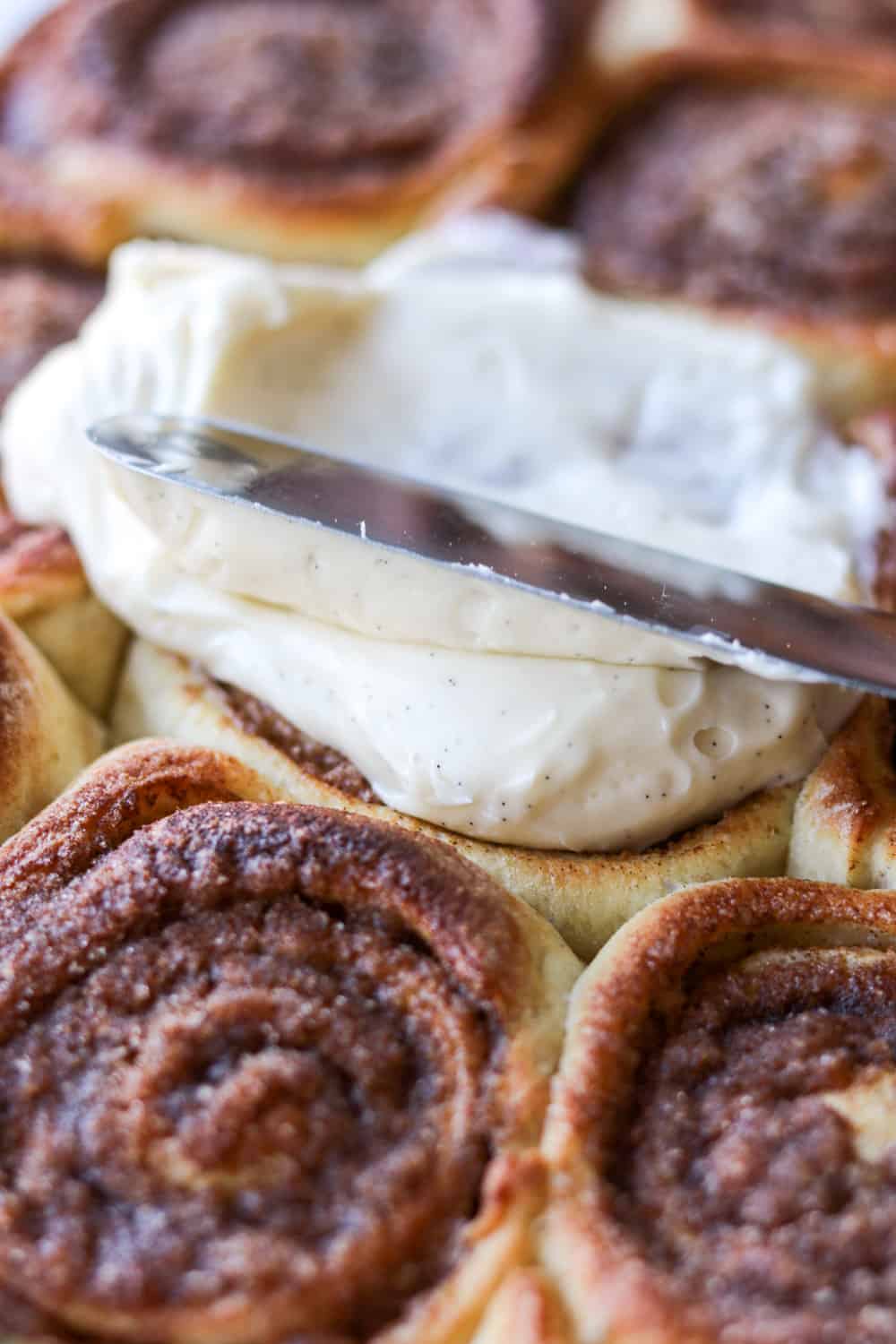 Spreading Vanilla Bean Frosting on a cinnamon roll.