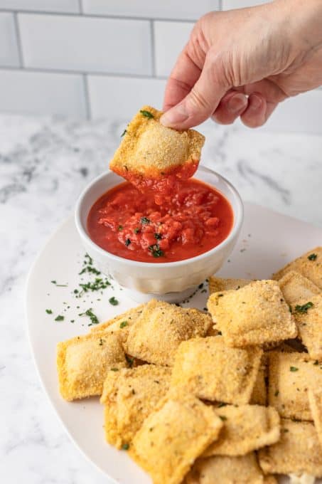 Dipping breaded ravioli into marinara.