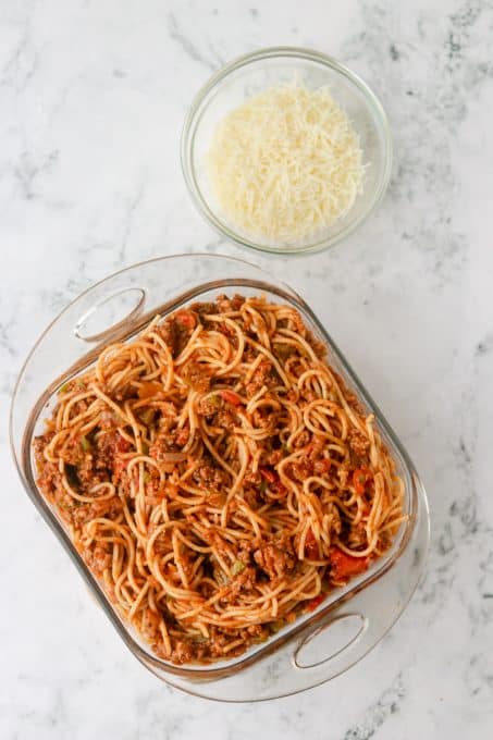A baking dish of spaghetti with meat sauce and mozzarella cheese ready to be baked.