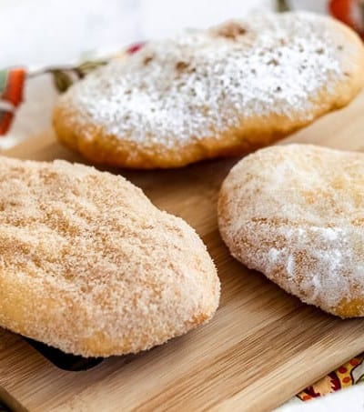 Three doughboys or fried dough coated in sugars on a cutting board.