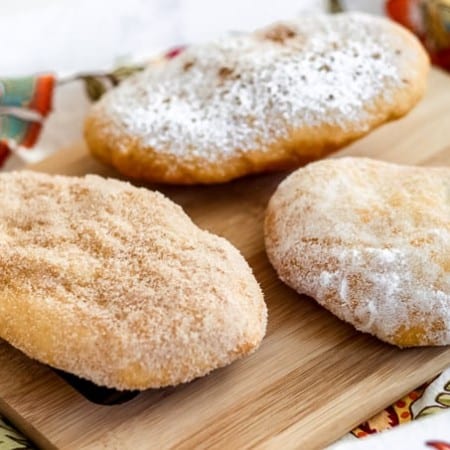 Three doughboys or fried dough coated in sugars on a cutting board.