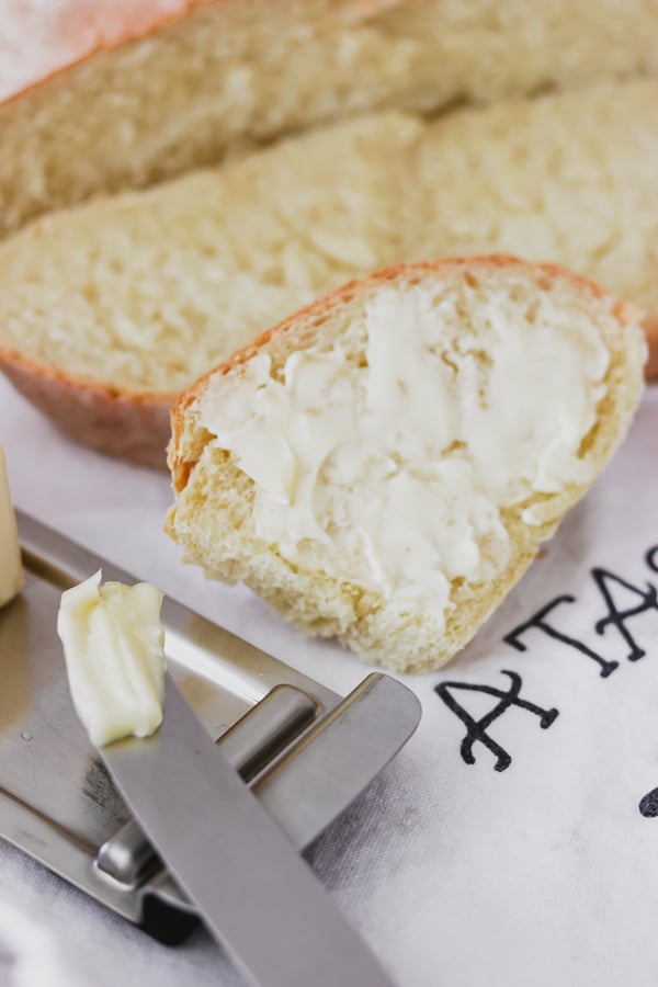 A slice of buttered Grandma's Italian Bread with butter on the knife.