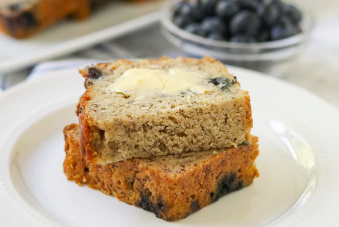 A buttered slice of quick bread with blueberries in the background.