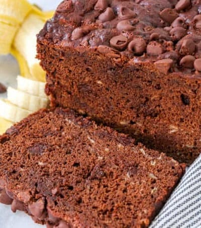 A loaf and slice of Double Chocolate Banana Bread on a marble cutting board.