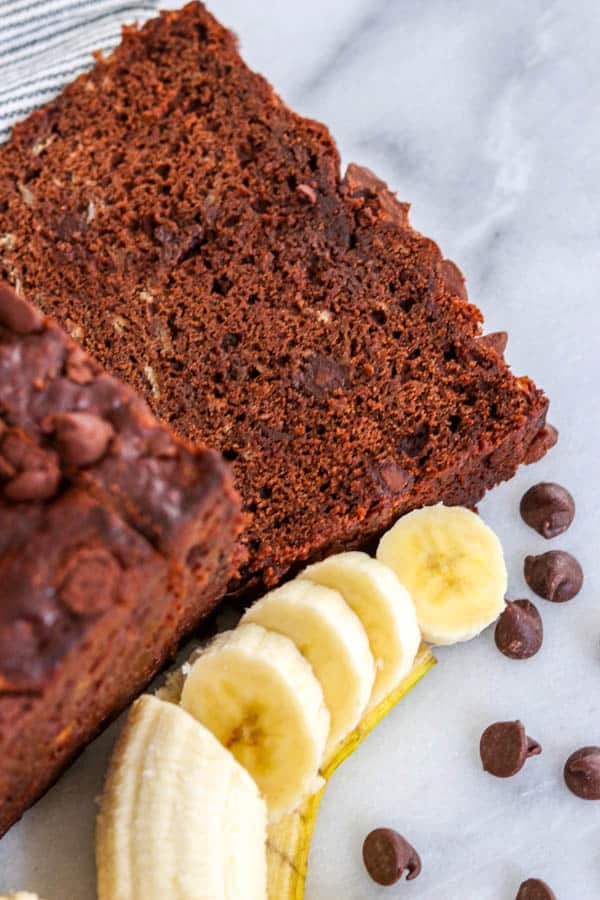 A slice of Double Chocolate Banana Bread next to a sliced banana and chocolate chips.