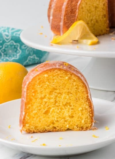 A piece of classic Easy Lemon Cake on a plate with lemons for a potluck.