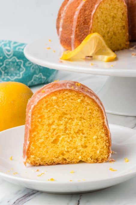 A piece of classic Easy Lemon Cake on a plate with lemons for a potluck.