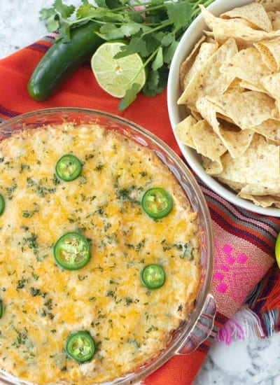 A plate full of taco dip and a bowl of tortilla chips.