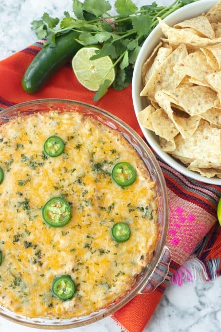 A plate full of taco dip and a bowl of tortilla chips.