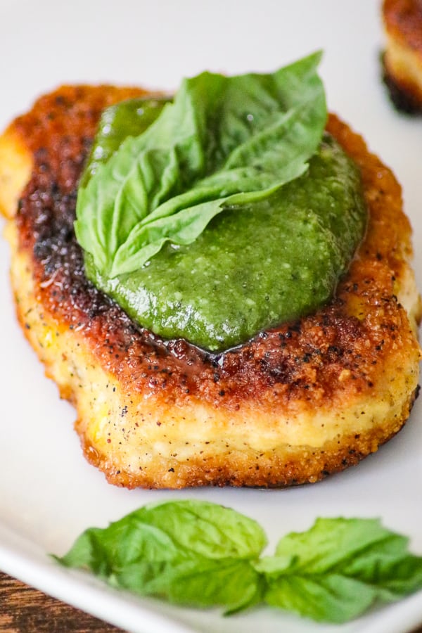 Parmesan Pork Chops with Pesto topped with pesto and a basil leaf.