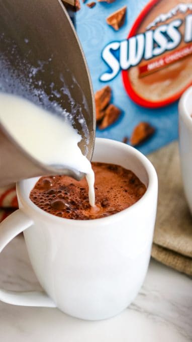 Pouring warm milk into mugs to make Chocolate Covered Cherry Hot Chocolate.