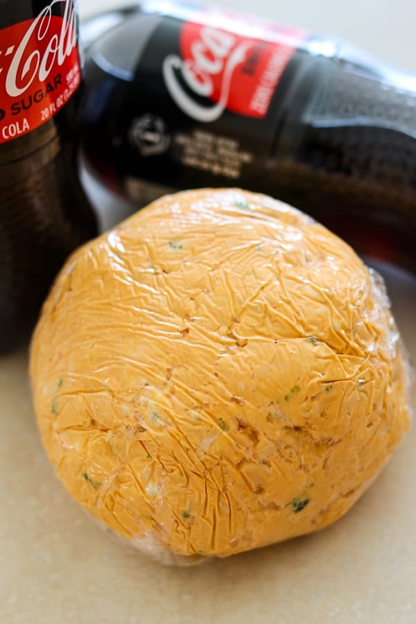 Buffalo Chicken Cheese Ball wrapped in plastic wrap with Coca Cola Zero.