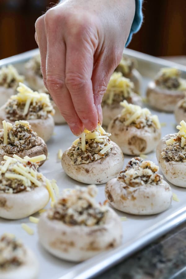 Adding Kerrygold Savory Shredded Cheddar to Cheesy Sausage Stuffed Mushrooms.