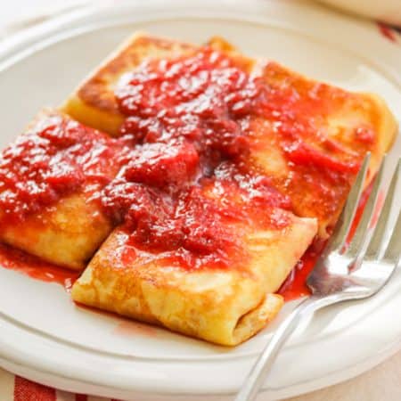 A plate of blintzes covered in strawberry sauce.