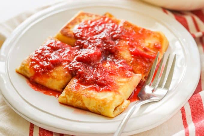 A plate of blintzes covered in strawberry sauce. 
