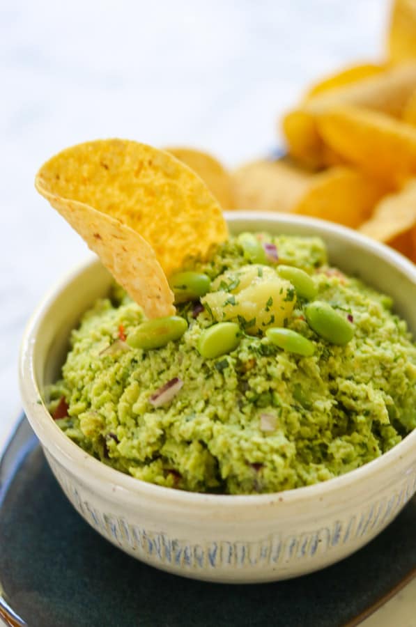 A tortilla chip stuck in edamame guacamole.