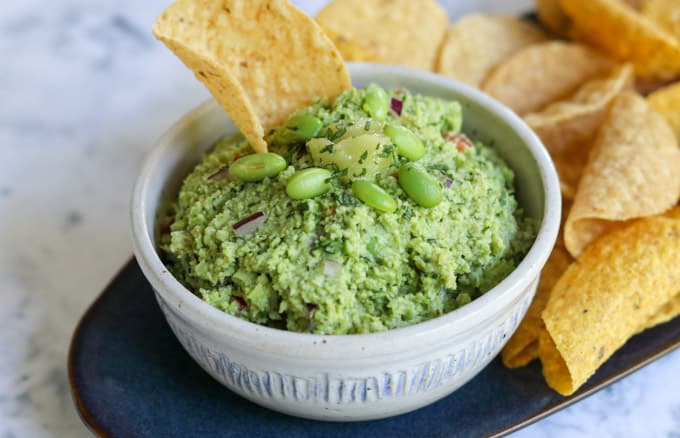 A chip in guacamole topped with edamame.