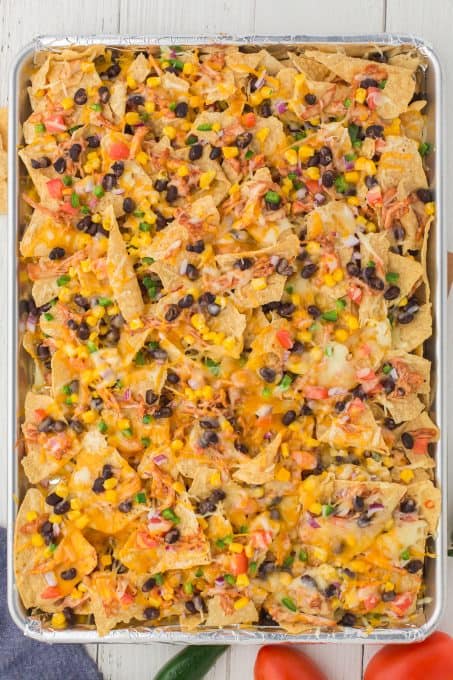 A tray full of loaded nachos with shredded chicken.