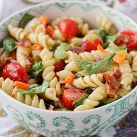 A bowl full of salad with bacon, pasta, orange pepper, red onion, cherry tomatoes, Romaine lettuce and ranch dressing.