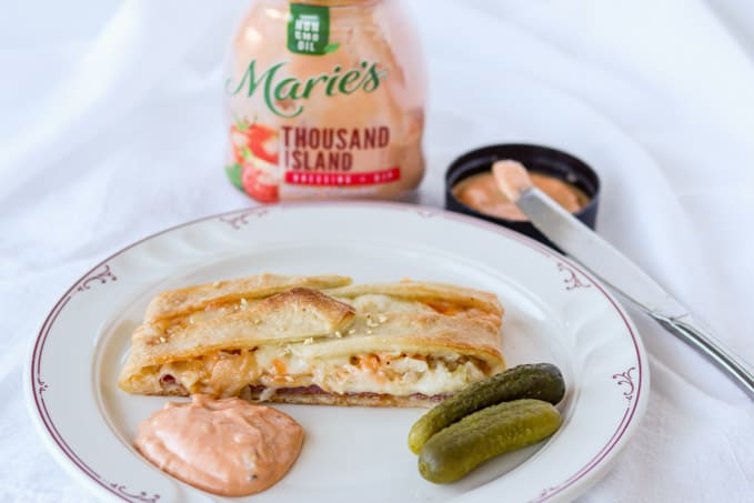 A plate with pickles, Marie's Thousand Island Dressing and a Reuben Braid slice.