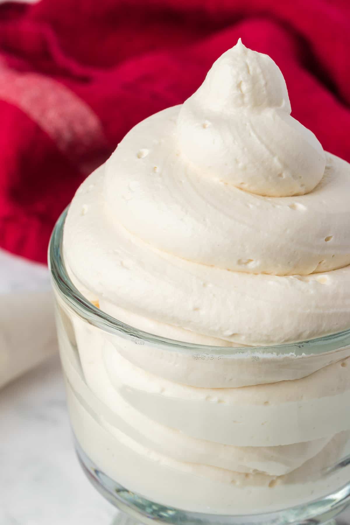 Piped Stabilized Whipped Cream in a glass serving dish in front of a red napkin.