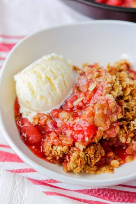A bowl of strawberry rhubarb dessert with a scoop of ice cream.