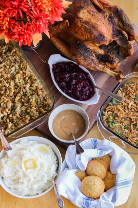 A Thanksgiving spread with turkey, stuffing, mashed potatoes, green beans, cranberry sauce, gravy, and rolls