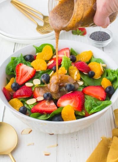 Pouring a poppy seed dressing onto a spinach salad.