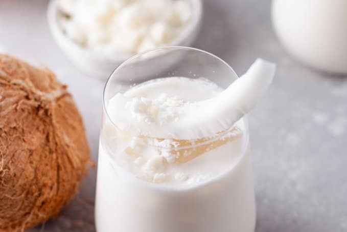 A glass full of a coconut drink with a piece of coconut.