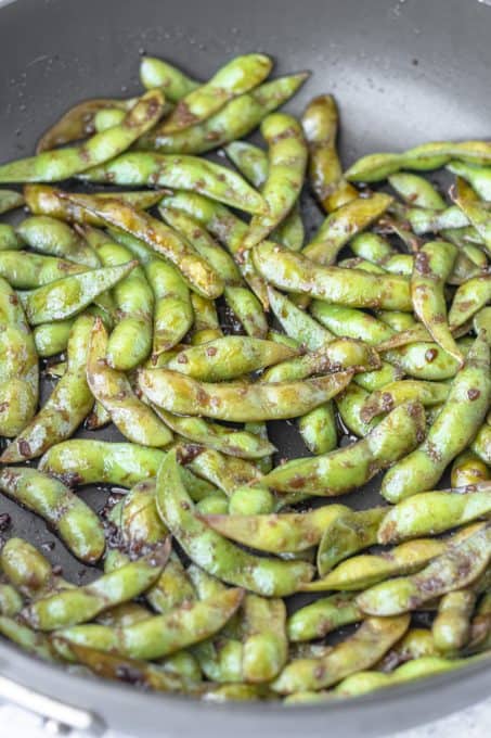 Edamame being sautéed in soy sauce, garlic, and salt.