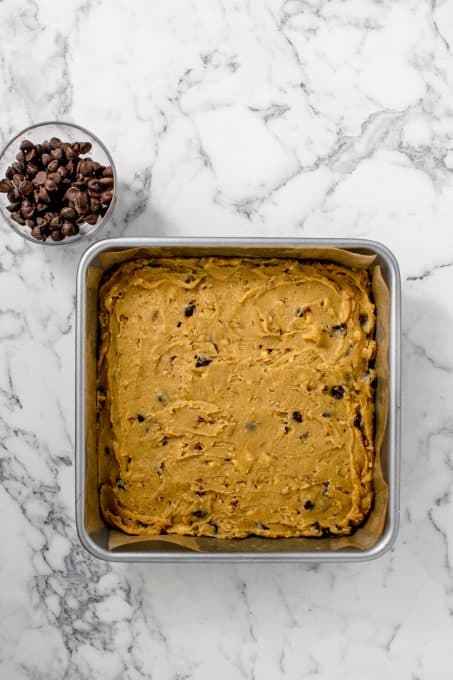 A baking pan with blondies ready for the oven and a bowl of chocolate chips.