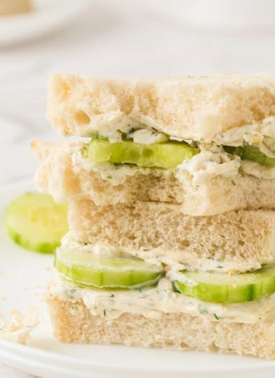 A bite taken out of a sandwich of cucumbers and cream cheese.