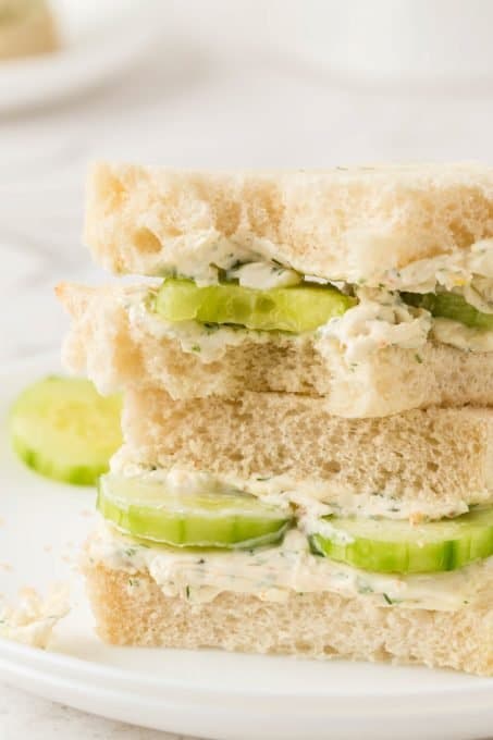 A bite taken out of a sandwich of cucumbers and cream cheese.