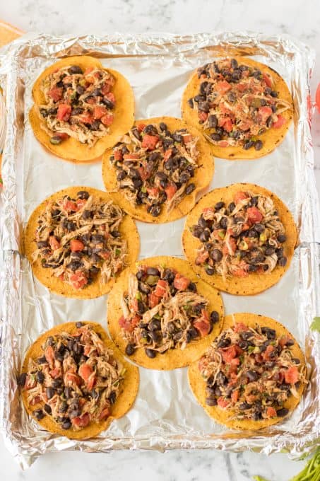A filling of chicken, beans cheese and tomatoes on top of crispy tortillas ready for the oven.