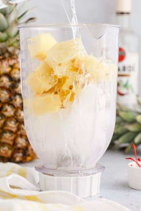 Ice, rum, and pineapple in a blender to make a pineapple coconut rum cocktail.