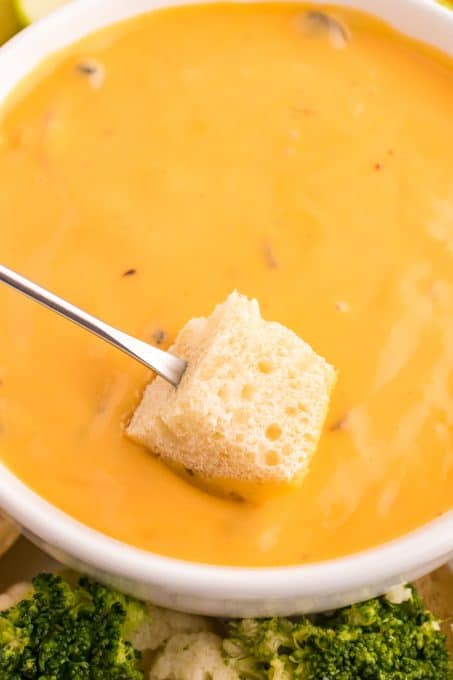 A cube of bread on a fondue fork being dipped into cheese.