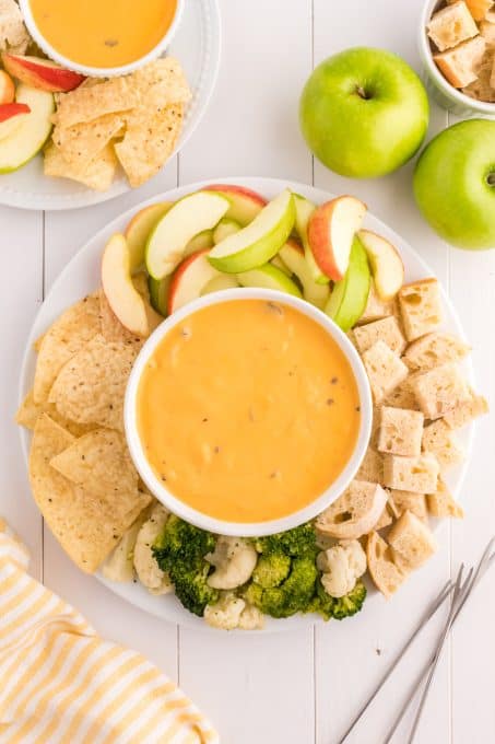 A bowl of fondue with cheese surrounded by dippers.