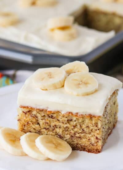 A slice of cake made with bananas topped with a frosting and banana slices on a plate.