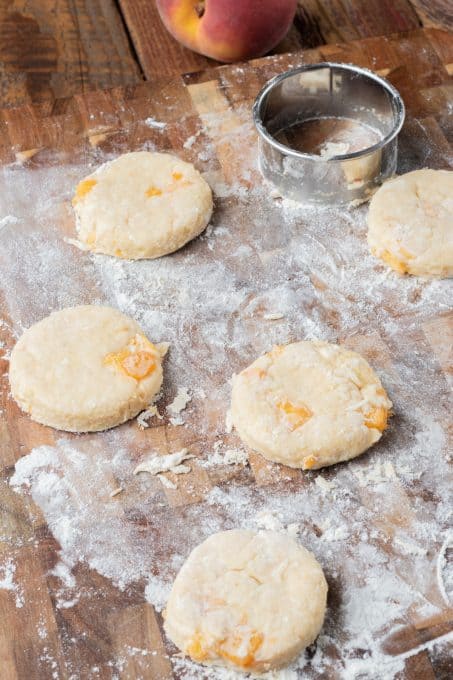 Scone dough on a floured board with pieces of peach inside.
