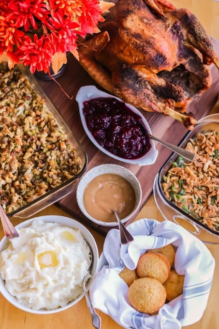 A Thanksgiving spread with turkey, stuffing, mashed potatoes, green beans, cranberry sauce, gravy, and rolls.